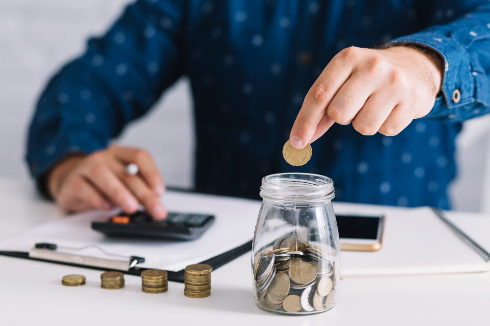 close up man s hand putting coin jar using calculator 1