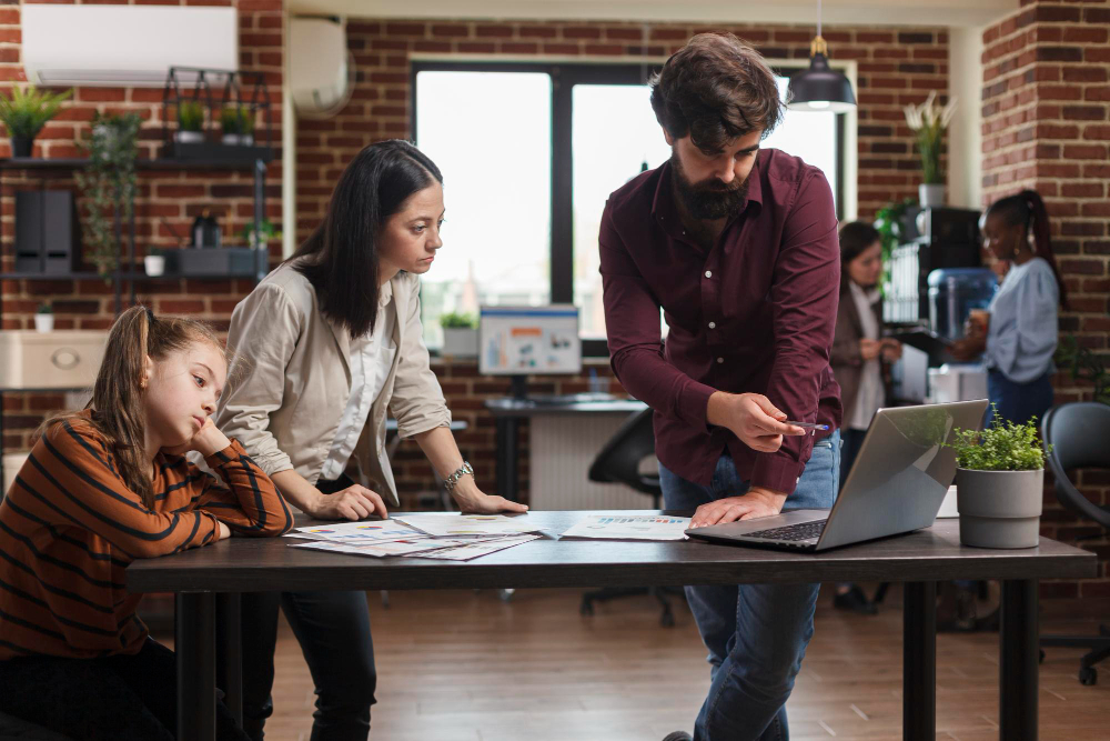 working mother reviewing financial agency paperwork while daughter is bored young busy businesswoman analyzing company documentation while coworker pointing wrong accounting data