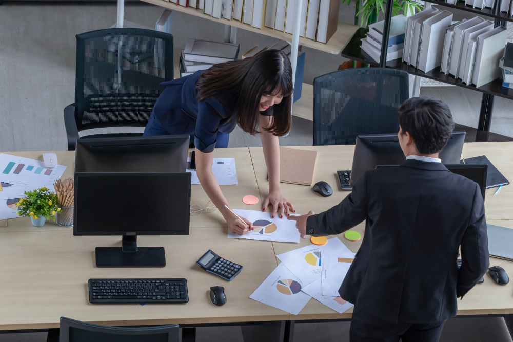 young businessman is describing job beautiful asian woman wearing dark blue suit desk modern office