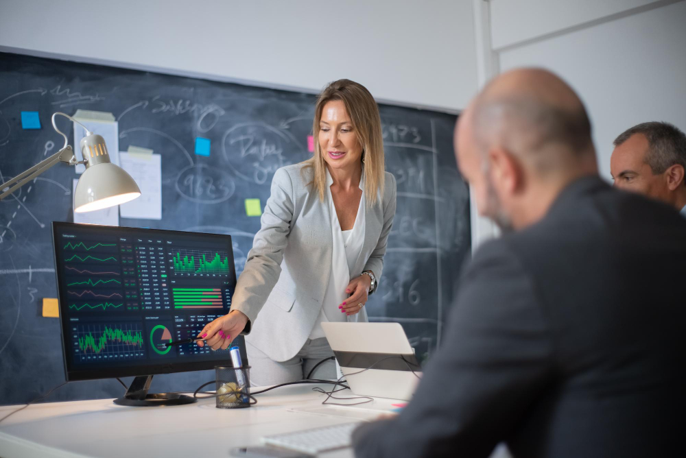 company employees discussing market data charts skilled woman leader two men looking diagrams computer screen analyzing profit growth business growth female business leaders concept