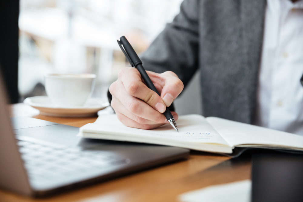 cropped image businessman sitting by table cafe with laptop computer writing something